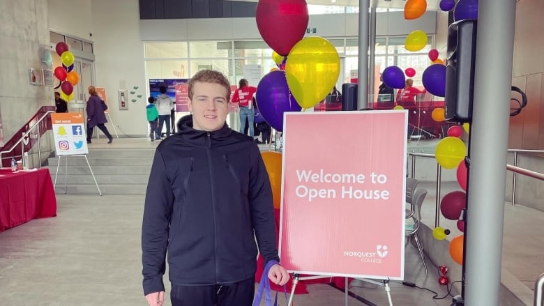 A young man stands next to a red sign that says 