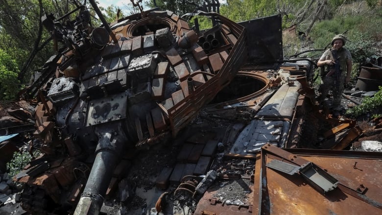 A Ukrainian soldier stands near a destroyed tank in Ukraine's Donetsk region on Thursday.