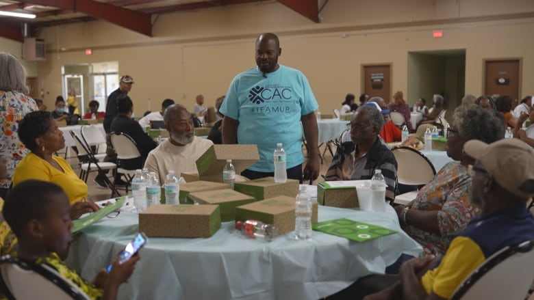 A man in a blue T-shirt stands at a table of people sitting.