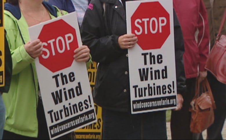 Close-up of signs held by two people that say 'Stop the wind turbines!'  