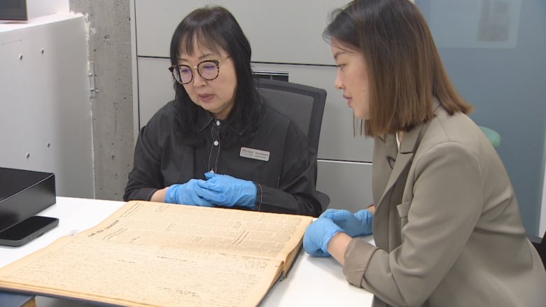 Two women looking at a book in a archive room. 