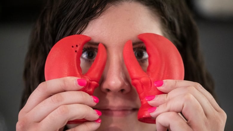 A woman holds two salt and pepper shakers shaped like lobster claws to her face, with the claws seeming to cover her eyes.