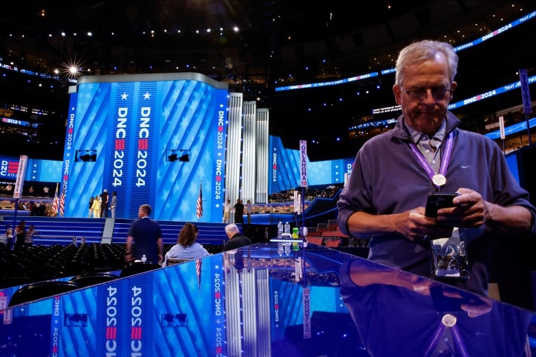 Man looks at phone near big shiny blue stage that says DNC 2024