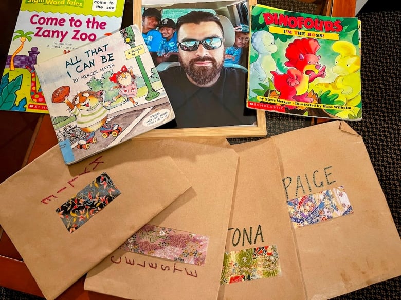 Children's books and envelopes with kids' names on them are spread on display, around a framed photo of a man.