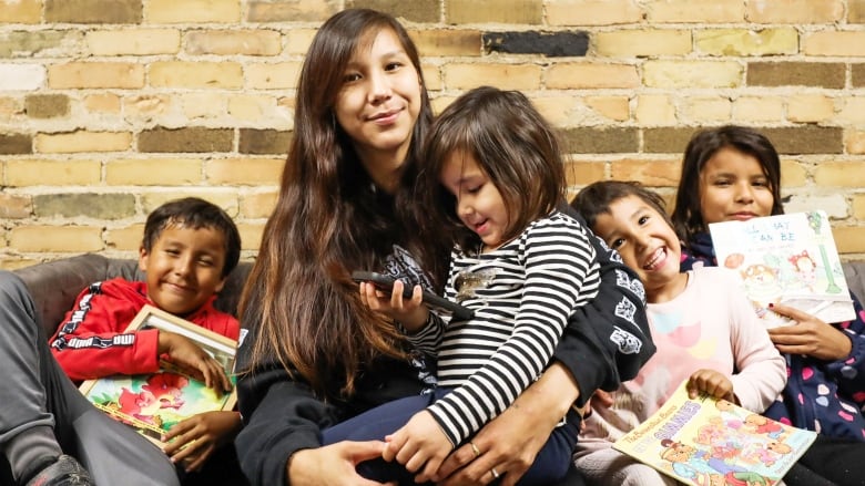 A woman sits on a couch and is surrounded by kids holding storybooks.