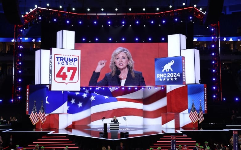 A woman speaks at a podium while a larger image is projected on a screen above her. 