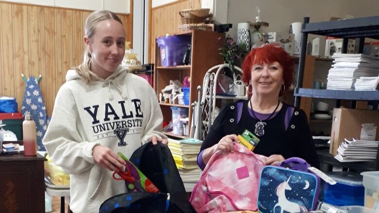 Two women stand in front of colourful supplies for school. 