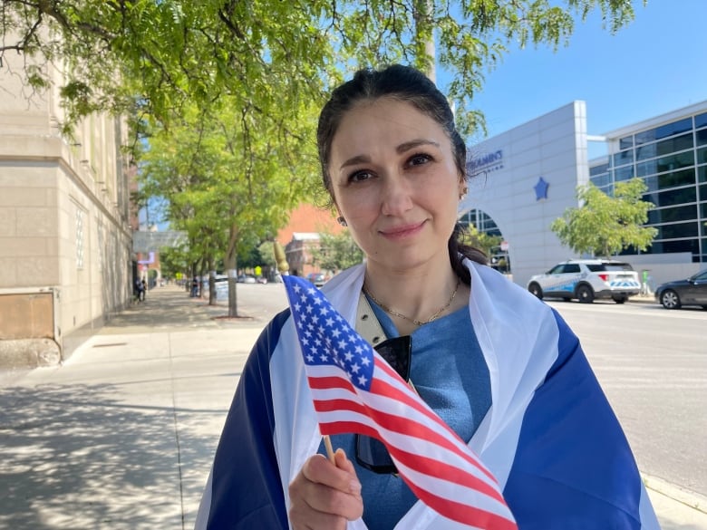 A woman holds a small U.S. flag and wears an Israeli flag wrapped around her shoulders.