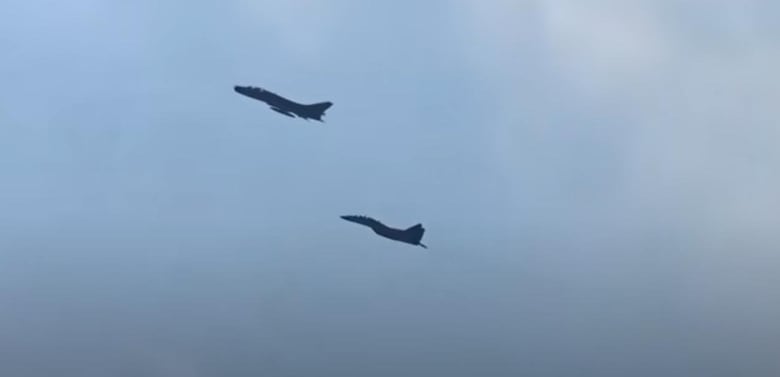 A dark image shows two fighter jets flying in a cloudy sky.