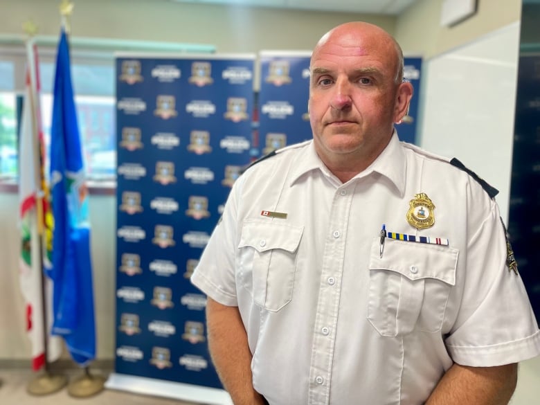 A man in a white police shirt stands with an expressionless face. 