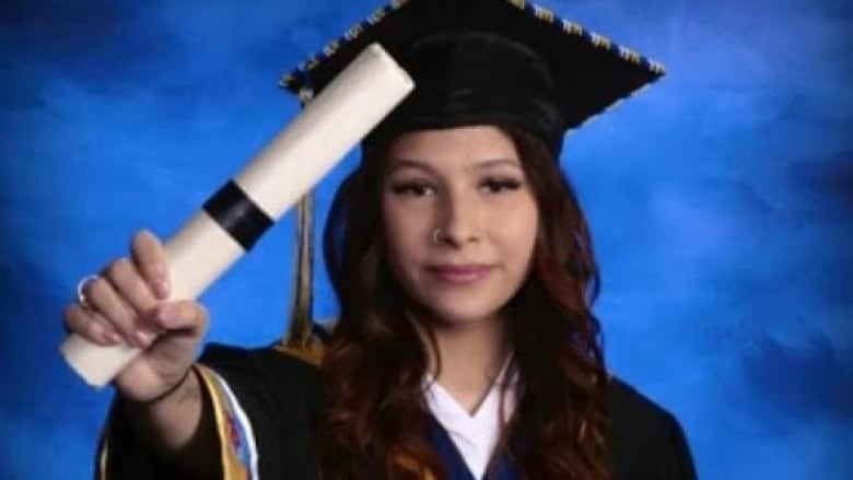 A woman holding her degree in a graduation cap and gown. 