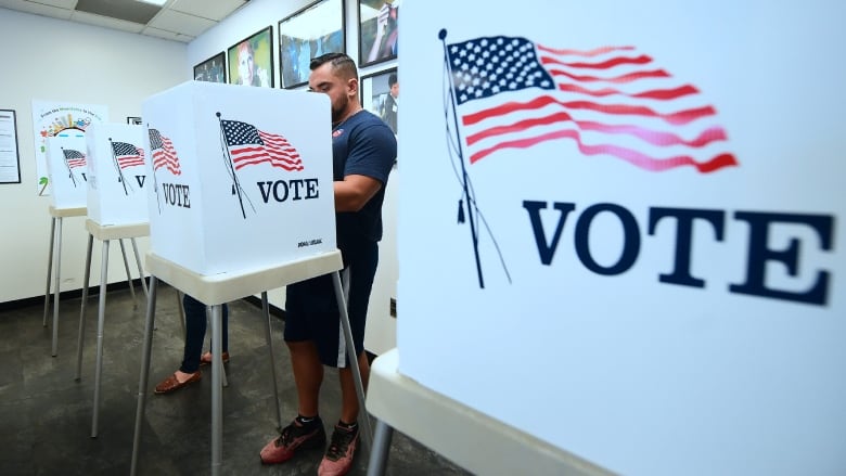 A man stands behind a partition with an image of the American flag that reads 'vote.'