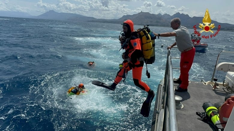 A diver in a red suit jumps off a boat into the ocean.