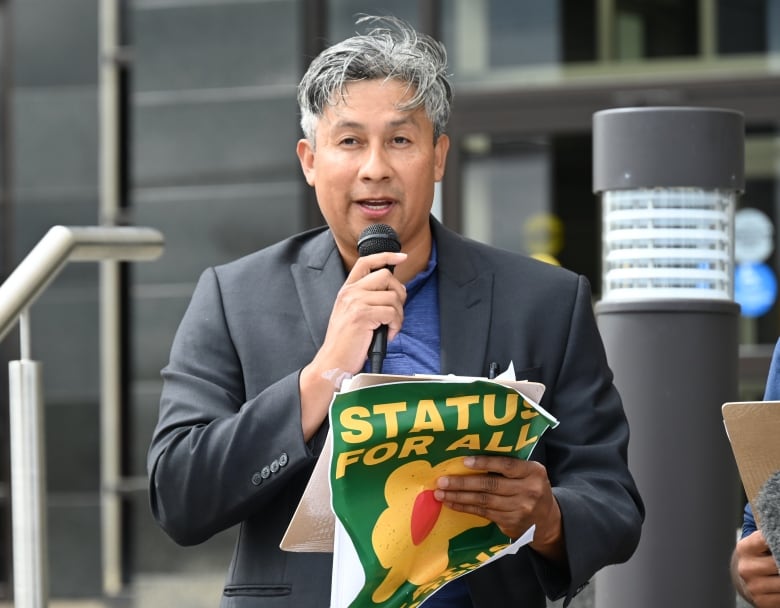 a man holds a clipboard, speaks into a mic