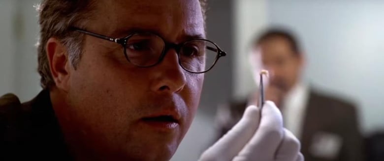 Man in glasses stares at a maggot that he is holding up with tweezers.