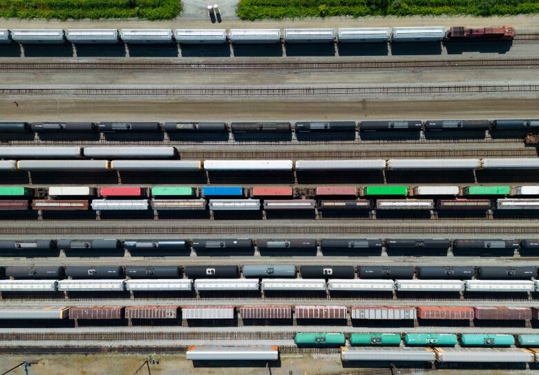 A locomotive, top, moves rail cars as others sit idle along with tanker cars and shipping containers 