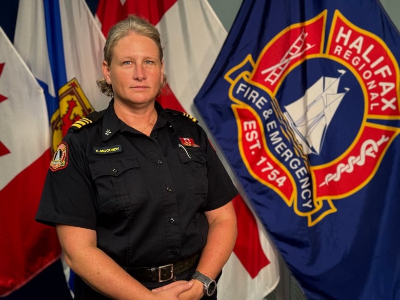 A woman in firefighter uniform stands in front of flags. 