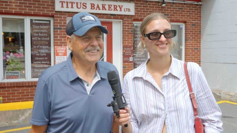 A smiling man with a moustache, wearing a blue T-shirt and baseball cap, with a younger smiling woman with blond hair, wearing dark sunglasses. 