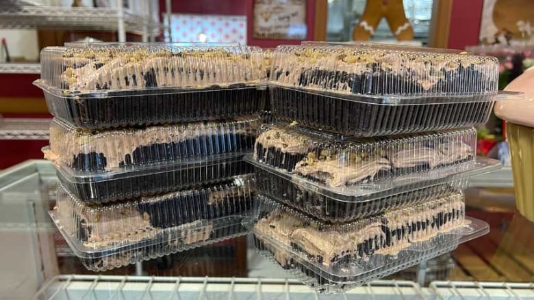 Two piles of three plastic containers of chocolate cake.