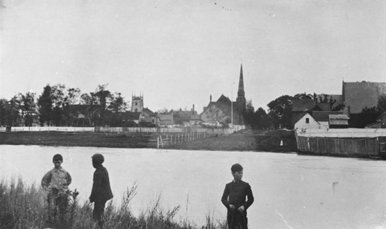 Old photo of pond with church steeple in background.