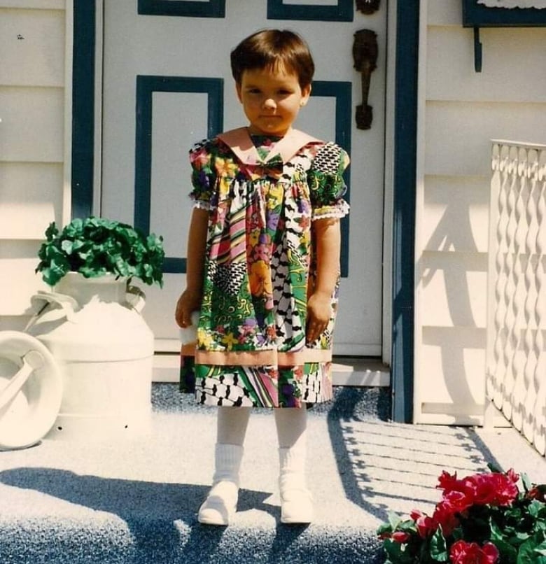 A little girl in a colourful dress in front of a door with a wreath. 