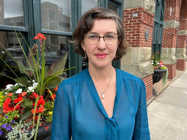 Woman with glasses and a teal blouse stands on a city street.