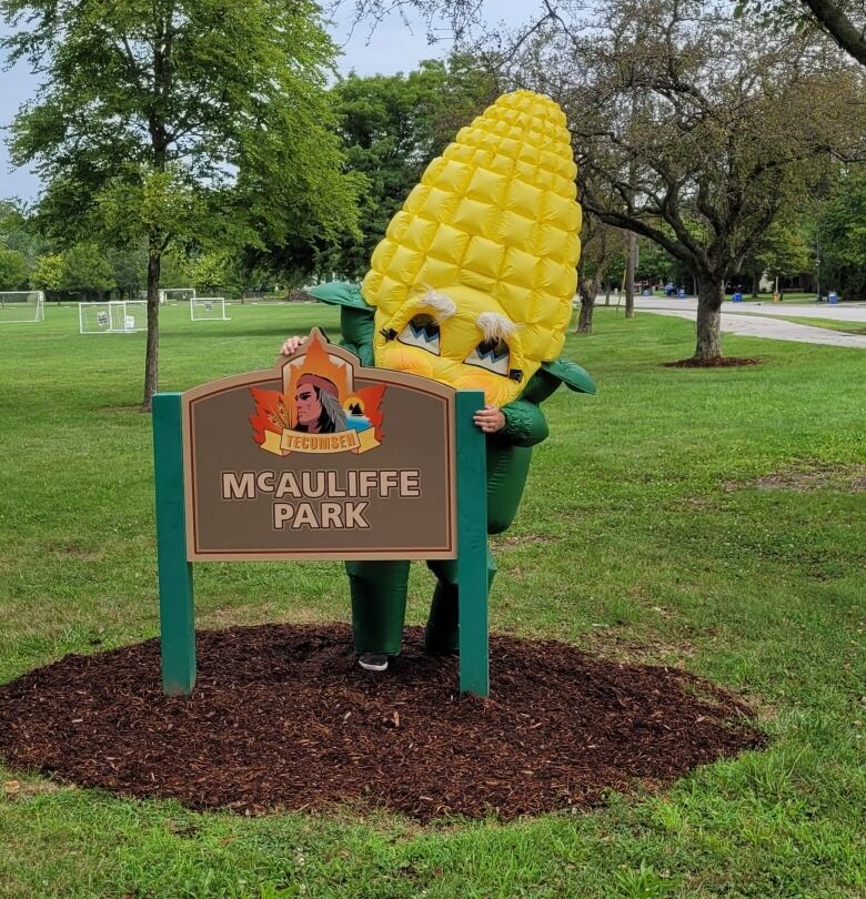 A costumed mascot stands next to a park sign.