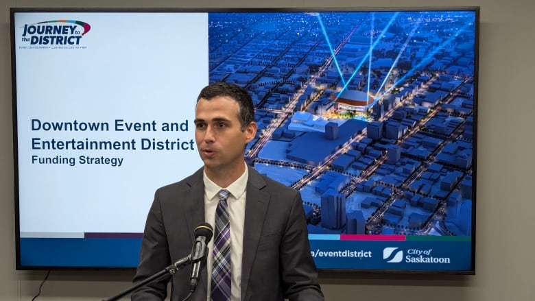 A man in a suit and tie in front of a powerpoint