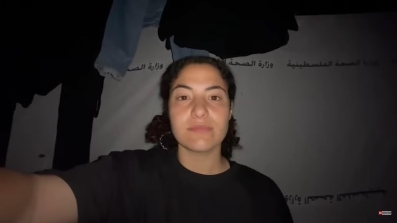 A woman films herself inside a dark tent.