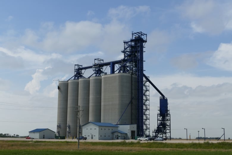 A grey grain elevator with a blue sky and clouds out in the country. 