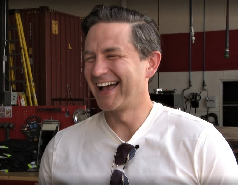 Pierre Poilievre, smiling, with a wall full of tools behind him.