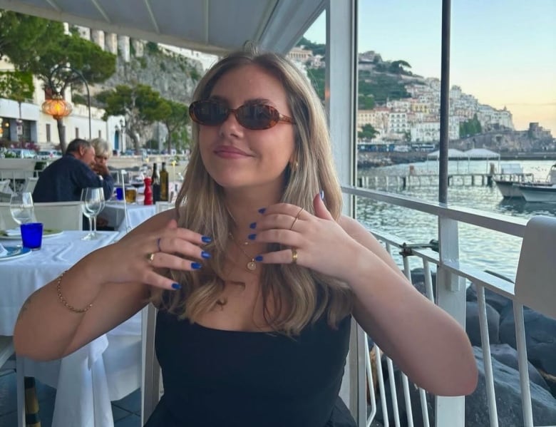 A woman in sunglasses sits on a patio by the sea