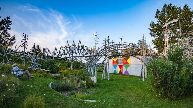 A man sits on a bench outside near a network of cement sculptures that resembles a rollercoaster track. 