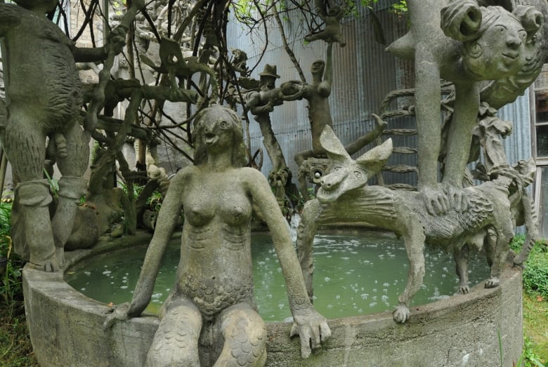 Cement sculptures depicting a mermaid and other mythical beasts surround a small pool of water outside a building. 