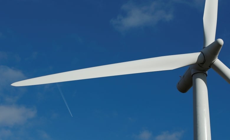 White wind turbine with axle far to the right and one turbine taking up most of the frame with blue sky in the background