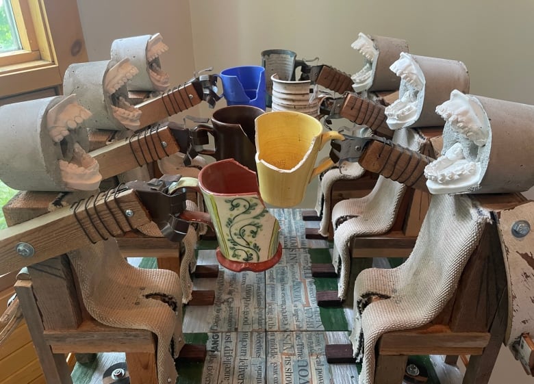 A small sculpture made of various scrap materials depicts six figures with cast jaws clinking tea cups in a cheers gesture. 