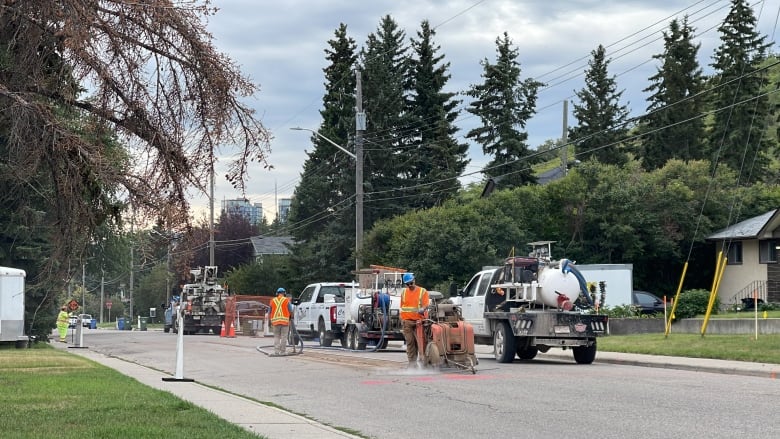 construction workers cut into a residential road. there are multiple large trucks and multiple people working.