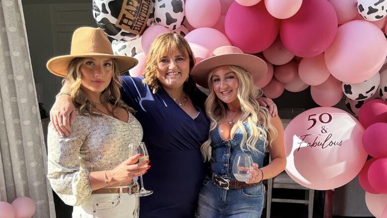 Three women standing in front of pink balloons. 