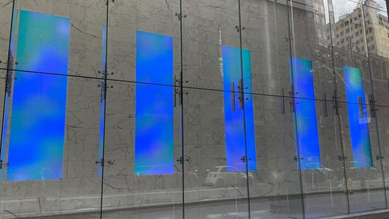 Straight Flush, a 2009 light installation by James Turrell, can be seen from sidewalk on Toronto's Adelaide St. W. Through windows, five tall rectangular screens are visible. All are beaming blue light.