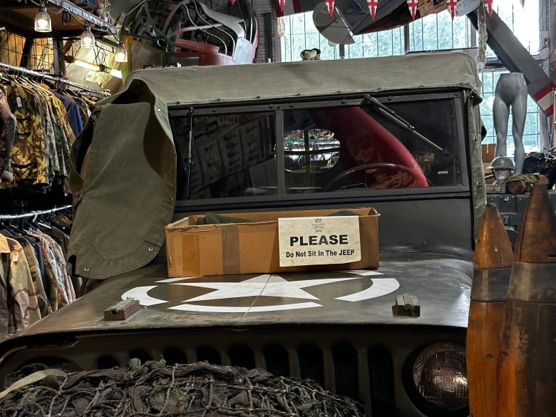 A dark green Jeep draped in green cloth sits in a store surrounded by various shirts and other military gear. A sign that reads 