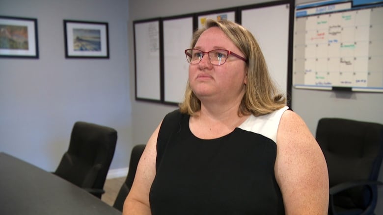 A woman with medium-length blonde hair wears glasses and a black shirt while looking off camera.