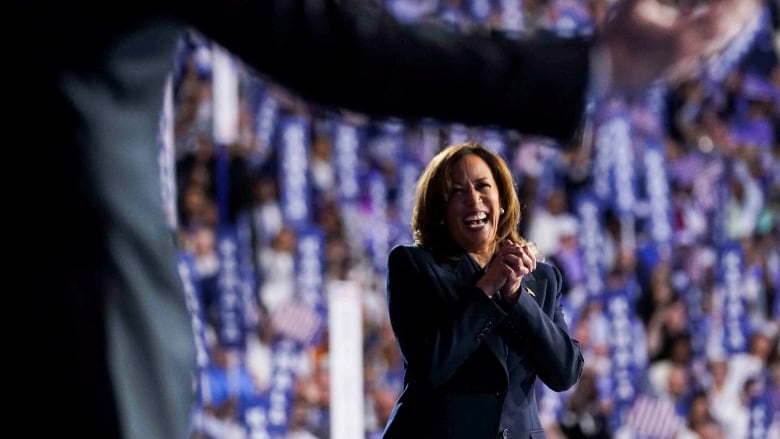 Harris, smiling with hands clasped on stage