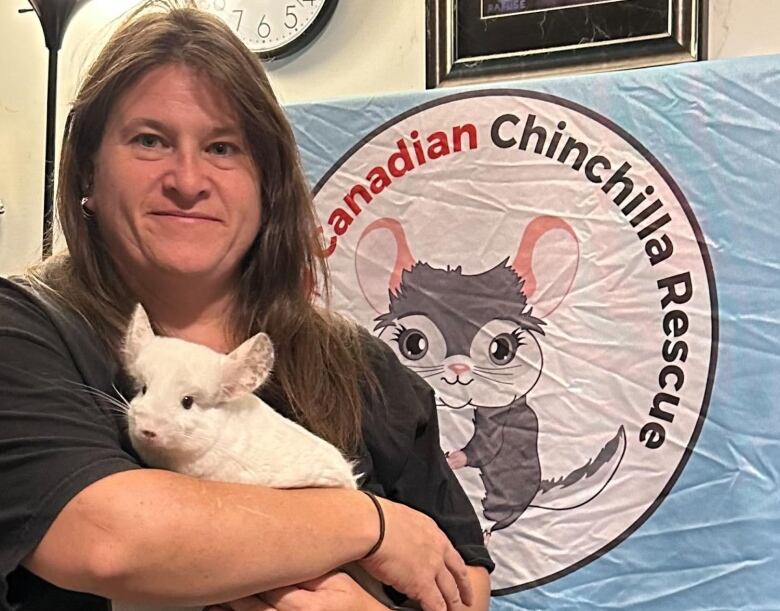 A woman, the founder of Canadian Chinchilla Rescue, holding one of her chinchillas with the Canadian Chinchilla Rescue logo in the background.