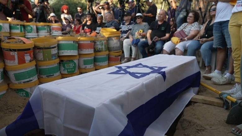 Mourners sit near a coffin covered in an Israeli flag.