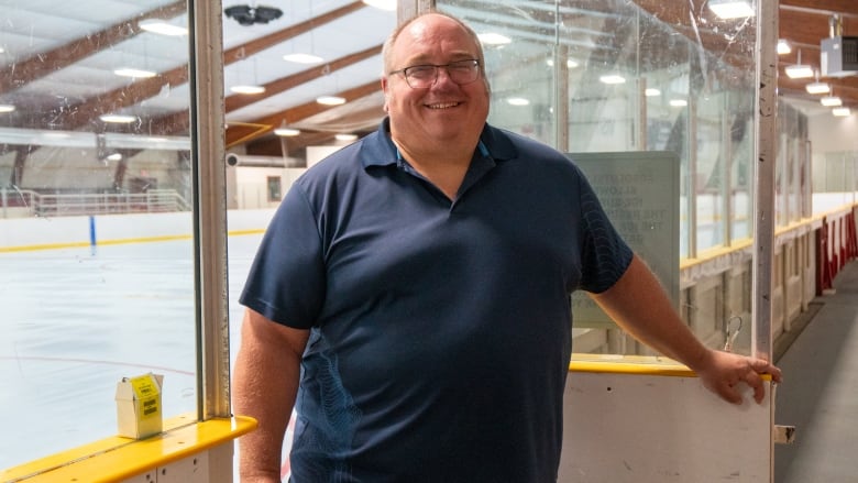 A person wearing a blue golf shirt is seen standing in the doorway of an ice rink.