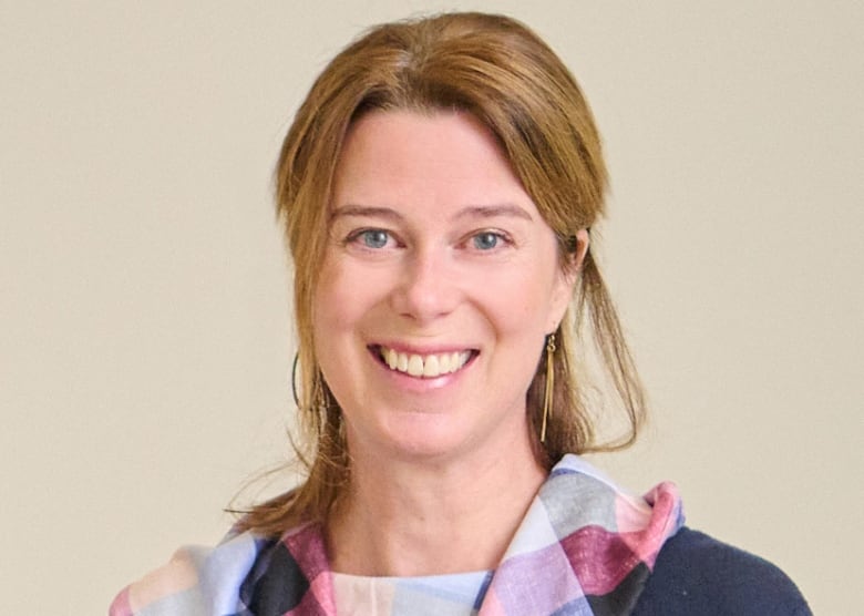 Woman smiling with reddish blonde shoulder-length hair, wearing a blue top with a multicoloured collar. 