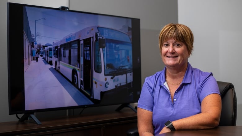 A woman sits a table with the picture of a bus in the background.