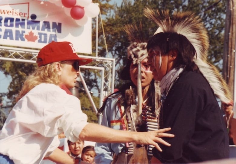 A woman in red camps with two individuals wearing headgears at an event.