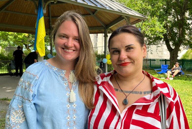 Two women stand next to each other and smile. In the background, there's a Ukrainian flag.