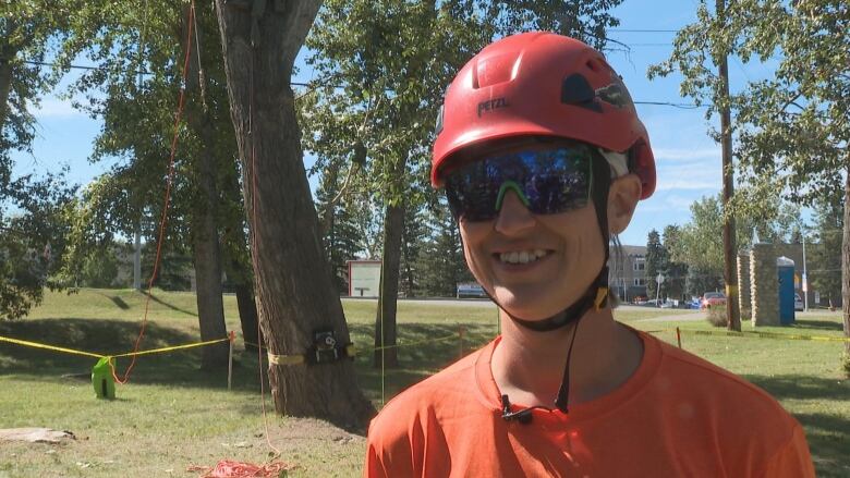 A woman wearing a red helmet, blue sunglasses and an orange shirt.